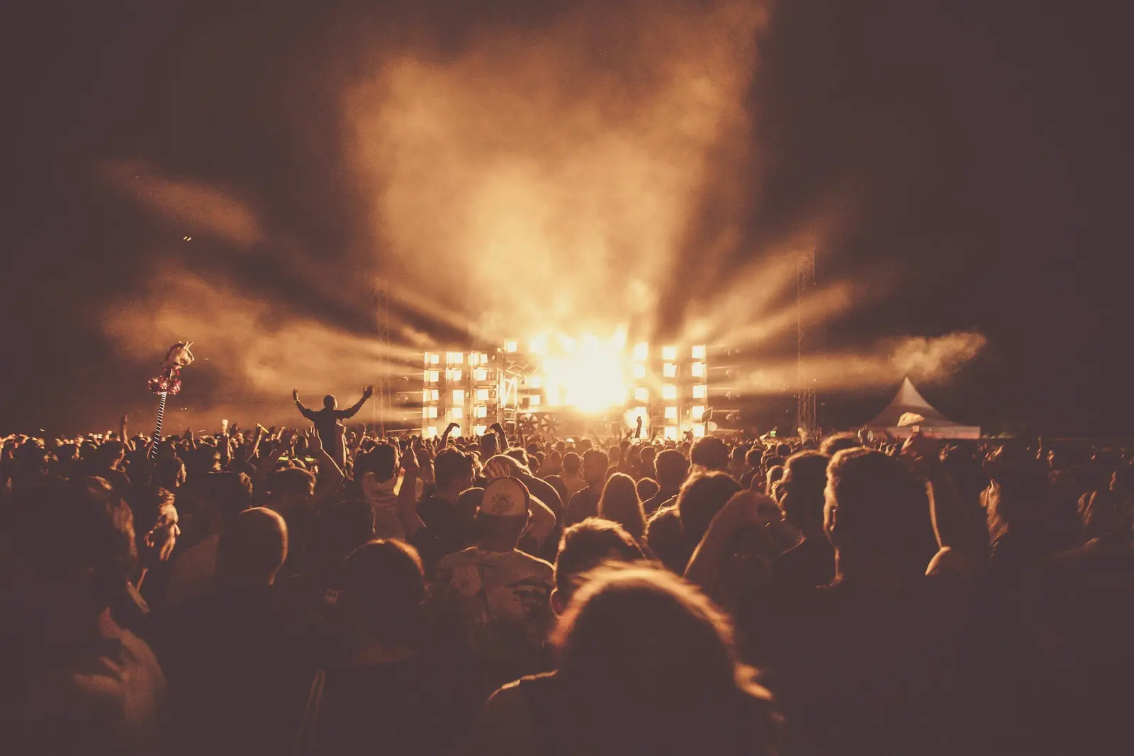 Silhouetted crowd facing a stage lit by bright beams