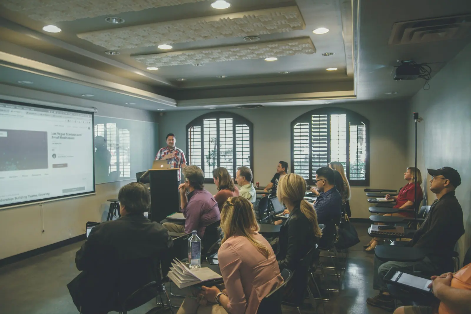 Participanți la seminar așezați pe rânduri, cu fața spre ecran